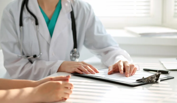 A doctor with her hands on a clip board talking to another person