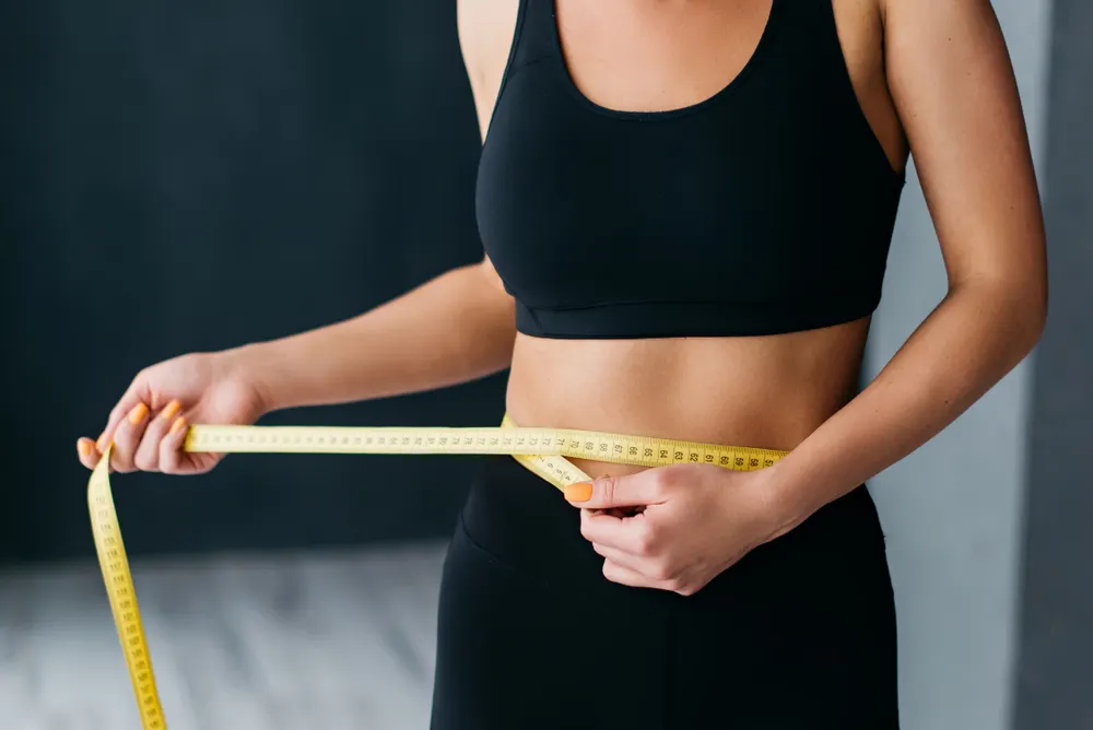 woman in sports bra measuring her waist with tape