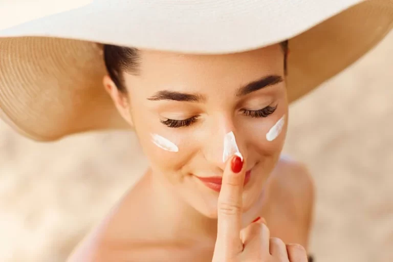 woman with sun hat and red nail polish with finger on nose