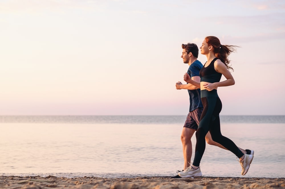 couple running along beach in workout clothing