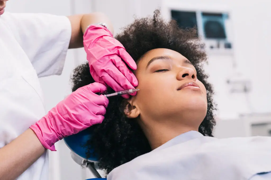 Attractive young African woman is getting a rejuvenating facial injections. She is sitting calmly at miami beach medspa getting botox injections.